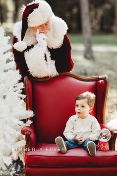 a little boy sitting in a red chair next to santa clause