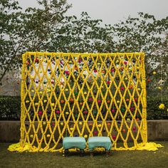 two blue benches sitting in front of a yellow latticed fence with flowers on it