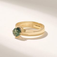 a gold ring with a green stone in the center on a white surface, it appears to be part of a jewelry set