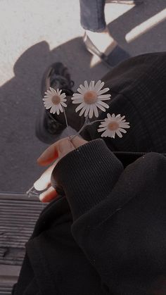 a person is holding flowers in their hand and looking down at the ground below them