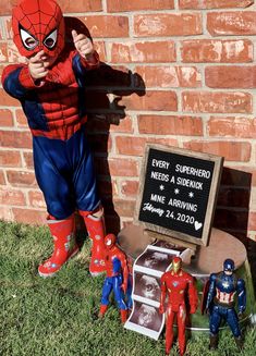 a spiderman statue next to a sign and some toy figurines on the grass