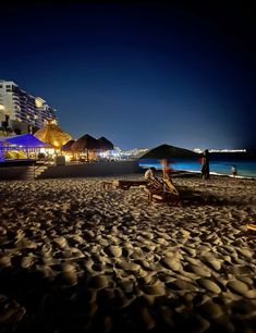 the beach is lit up at night with umbrellas and lounge chairs in the foreground