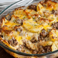 a casserole dish with meat, cheese and potatoes in it on a wooden table