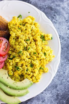 a white plate topped with eggs, tomatoes and avocado next to some bread