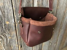 a brown leather purse hanging on the side of a wooden wall with an open pocket