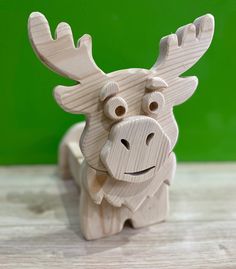 a wooden moose toy sitting on top of a wooden table next to a green wall