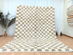 a white and brown checkered blanket sitting on top of a wooden floor next to a potted plant