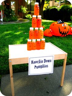 a table with pumpkins on it in front of a house and lawn, next to a sign that says halloween carnival games