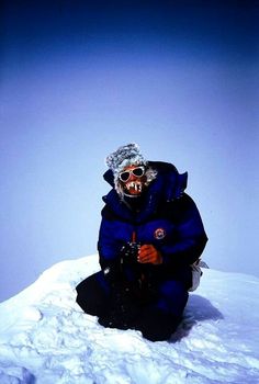 a man sitting on top of a snow covered slope wearing a blue jacket and black pants