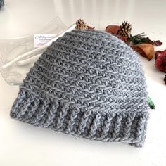 a gray knitted hat sitting on top of a white table next to dried flowers