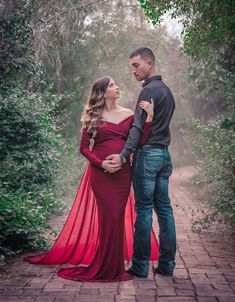 a pregnant woman in a red dress standing next to a man wearing a black shirt