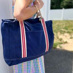 NEW! A rugged, coastal style tote perfect for hauling all your gear to the beach, boat, and beyond. The navy blue canvas with red striped trim is decidedly nautical and chic, and the grommets and leather trim add a refined touch. The natural rope handles are comfortable to carry, and the front pocket and interior zippered pocket keep your belongings safe and organized. 17" x 14". Large enough to carry everything you need throughout the day. Cotton Beach Bag With Braided Handles For Travel, Canvas Bag With Braided Handles For Daily Use, Everyday Canvas Bag With Braided Handles, Daily Use Canvas Bag With Braided Handles, Nautical Canvas Bags For Everyday Use, Navy Casual Canvas Bag With Large Capacity, Canvas Bag With Braided Handles For Everyday Use, Casual Navy Canvas Bag With Large Capacity, Navy Cotton Travel Bag