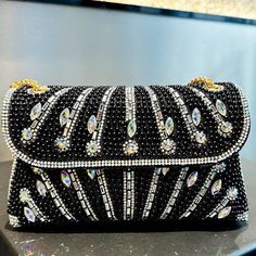 This stunning clutch is embellished with brilliant gem and rhinestone designs, producing a captivating design that catches the light and attention from every aspect. The Luciana Rhinestones Clutch Bag is designed to go well with a variety of ensembles and radiates a classic elegance that elevates any look. It is the ideal piece for special occasions because of its distinctive and striking appearance. For maximum comfort, this bag also includes a gorgeous gold chain strap. Now available in black, Chic Evening Bag With Bling For Night Out, Chic Embellished Crystal Bag, Chic Embellished Crystal Evening Bag, Glamorous Clutch With Rhinestones For Night Out, Rhinestone Clutch For Night Out, Crystal Clutch With Rhinestones For Party, Luxury Rhinestone Evening Bag For Party, Glamorous Rhinestone Clutch For Night Out, Chic Evening Crystal Bags