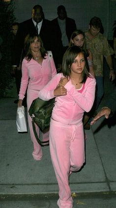 a woman in pink is walking down the street with other people behind her and carrying bags