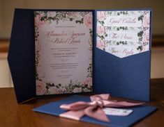 a wedding card with pink flowers on it and a blue pocketfolder next to it