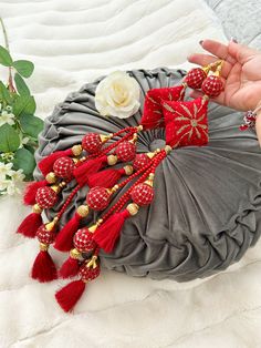 a woman holding onto a red and gold tasseled necklace on top of a gray pillow