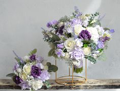 two purple and white flowers are in a vase on a shelf next to each other