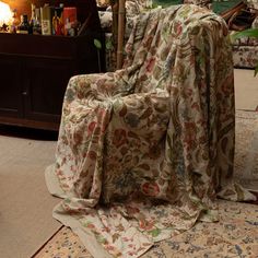 a chair covered with a blanket in front of a table and lamp on the floor