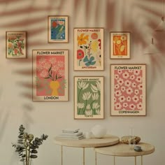 there are many posters on the wall above a table and vase with flowers in it