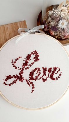 a cross - stitch pattern with the word love in red on it, next to a bowl of dried flowers