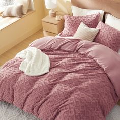 a bed with pink comforter and pillows in a bedroom