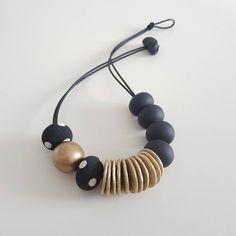 a black and gold necklace on a white surface with beads hanging from it's side