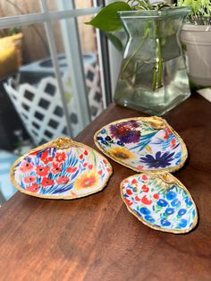 three decorative plates sitting on top of a wooden table next to a potted plant