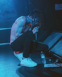 a shirtless man crouching down on the ground with his head in his hands