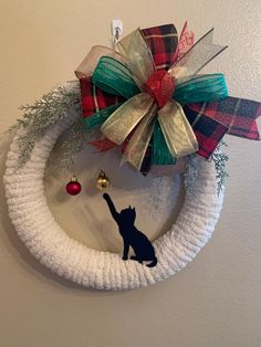 a wreath with a cat on it hanging from the wall next to a christmas ornament