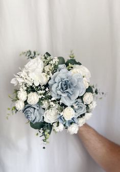 a bridal bouquet with blue and white flowers in someone's hand on a white background