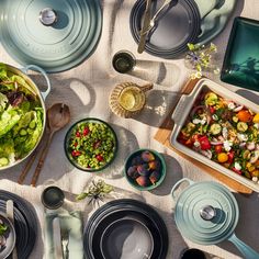 a table topped with lots of plates and bowls filled with food next to utensils