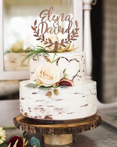 a white wedding cake with flowers on top sitting on a wooden stand in front of a mirror