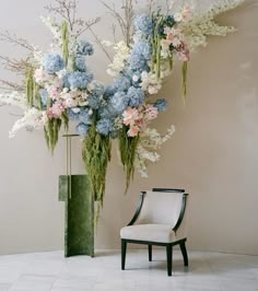 a chair sitting in front of a tall floral arrangement with blue and pink flowers on it