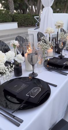 the table is set with black and white flowers in vases, silverware, and candles