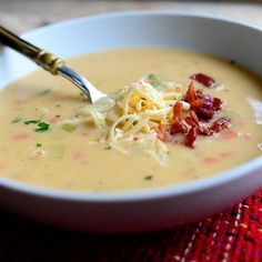 a white bowl filled with soup sitting on top of a red place mat next to a spoon