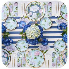 a table set with blue and white plates, silverware and flower centerpieces