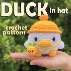 a small crocheted duck in a hat on someone's hand with trees in the background