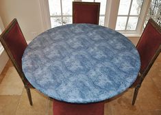 a round table with red chairs and a blue tablecloth on it in front of a window