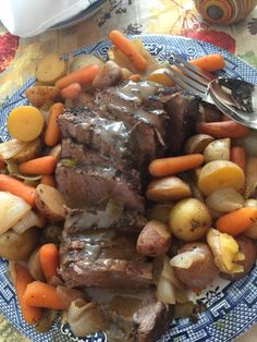 a blue and white plate topped with meat, potatoes and carrots next to a fork