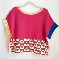 a pink top with brown and yellow designs hanging on a hanger next to a white wall