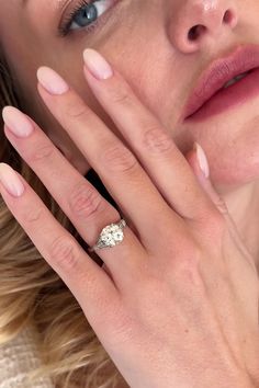 a close up of a woman's face with her hand near her face, wearing a diamond ring