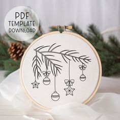 a hand embroidered christmas ornament hanging from a hoop with pine cones and bells