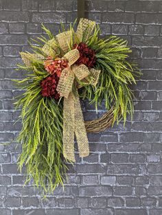 a wreath hanging on the side of a brick wall with greenery and red flowers