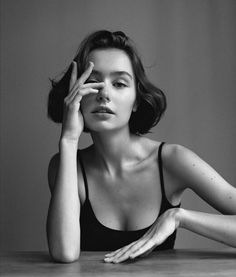 a black and white photo of a woman sitting at a table with her hand on her face