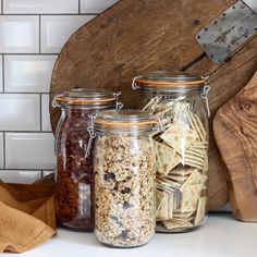 three glass jars filled with food sitting on top of a counter next to a cutting board