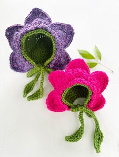 two crocheted flowers sitting next to each other on top of a white surface