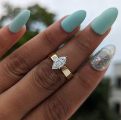 a woman's hand with blue manies and a ring on her finger, holding an oval shaped diamond