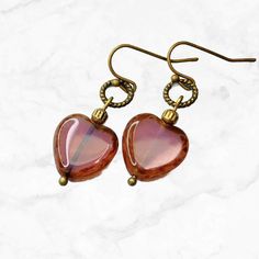 Beautiful tea rose pink Czech glass heart earrings. Picasso finish on the edges of the hearts, they dangle from small bronze rings. Elegant earrings that work for everyday wear or dressed up. Lightweight and comfortable. So pretty, this earring's color works well with pink, brown, beige, blue, green and more. Great with denim.  Hypoallergenic ear wires (nickel and lead free). Choose ear wire style at checkout. Artisan glass heart beads produced in small quantities in the Czech Republic.  Free Gi Heart Beads Metal Earrings For Gift, Metal Heart Beads Earrings For Gifts, Heart Beaded Metal Earrings As Gift, Heart Beads Metal Earrings As Gift, Metal Heart Beaded Earrings For Gifts, Metal Heart Bead Earrings As Gift, Gift Metal Heart Earrings With Heart Beads, Brass Heart Charm Earrings For Gifts, Brass Heart Charm Earrings As Gift