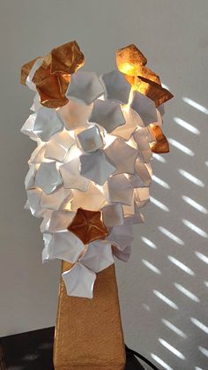 a sculpture made out of white and gold paper on top of a wooden table with sunlight coming through the window