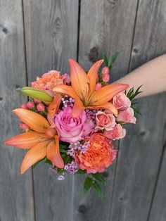 a bouquet of orange and pink flowers in front of a wooden fence with someone's hand holding it